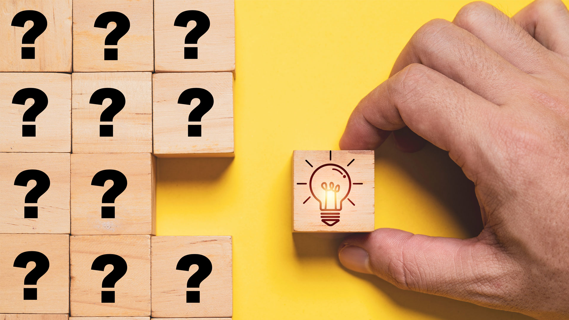 Blocks of question marks with a hand holding a block with a lightbulb icon in a yellow background