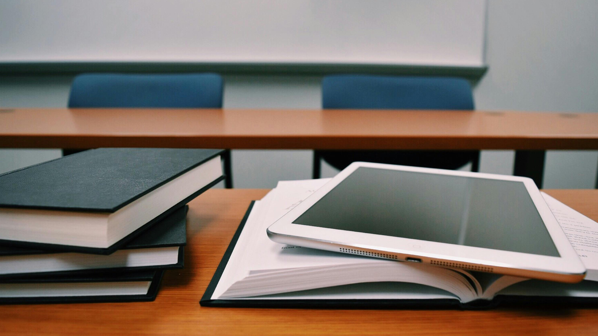 A desk with books stacked next to a open book with a tablet on top